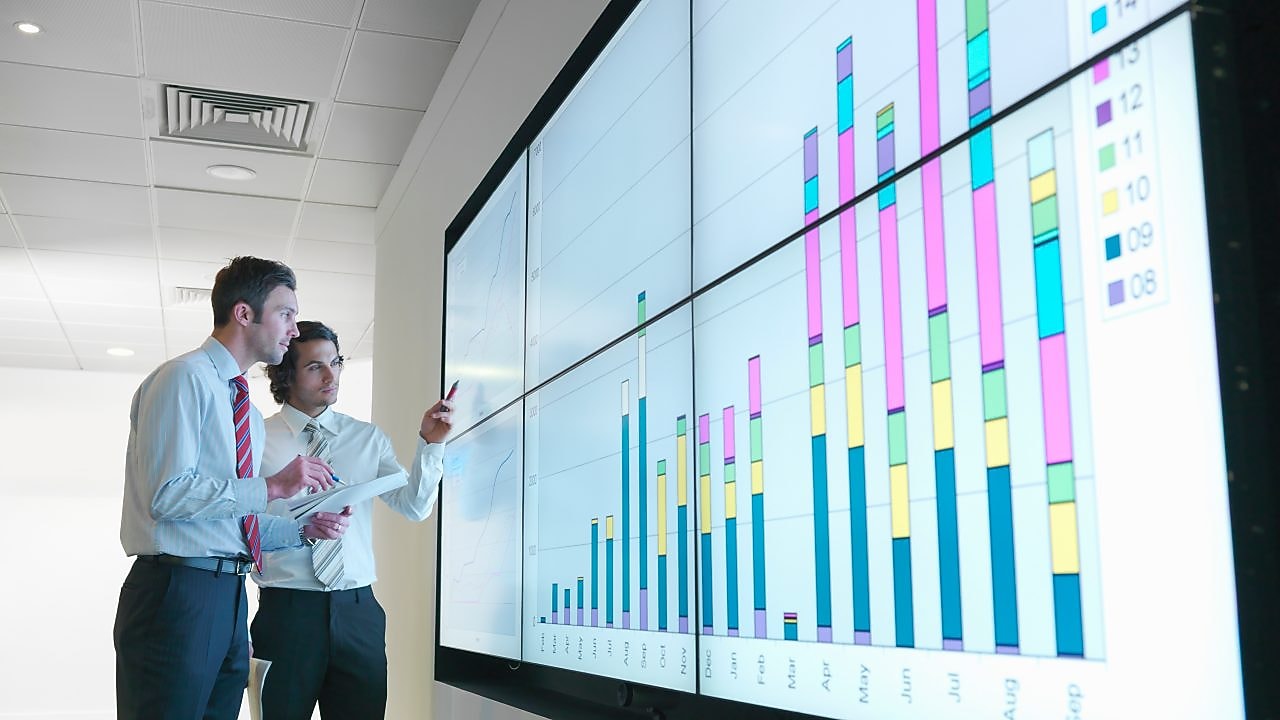 Business men analyse reports displayed on a large digital screen